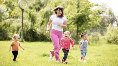 Kinder laufen mit Erzieherin im Kita-Garten