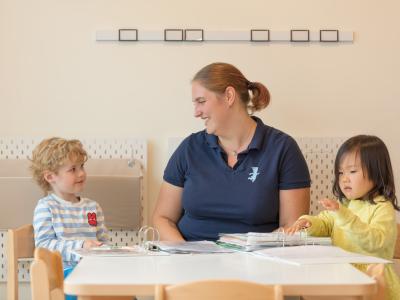 Eingewöhnung in der Kita Erzieherin sitzt mit Kindern am Tisch